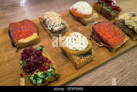 Una tavola di legno con una varietà di panini. I panini sono preparati con ingredienti diversi e sono disposti in modo visivamente accattivante. Foto Stock