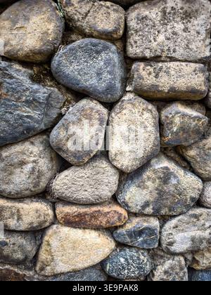 Primo piano dettagliato di un muro in pietra rustica realizzato con rocce dalla forma irregolare, che mostrano texture e colori naturali. Foto Stock