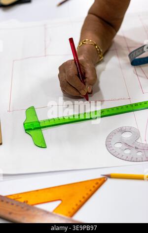 Uno scatto ravvicinato di un sarto disegna a mano su carta stampata con una penna rossa circondata da strumenti di precisione come un righello verde, una curva francese e l'arancione Foto Stock