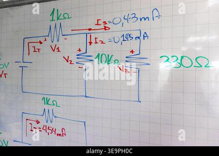 Primo piano degli schemi elettrici stampati a mano su una lavagna bianca a griglia. Visualizzazione dei resistori, dei simboli di tensione e dei calcoli della corrente per il motore Foto Stock