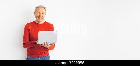 L'uomo sorride mentre tiene in mano il laptop in ambienti interni durante il giorno Foto Stock