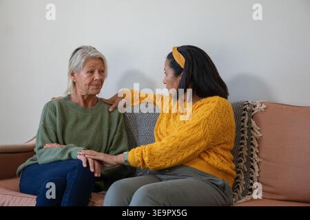 Donne anziane sedute vicine sul divano tenendosi delicatamente le mani indossando maglioni in maglia Foto Stock