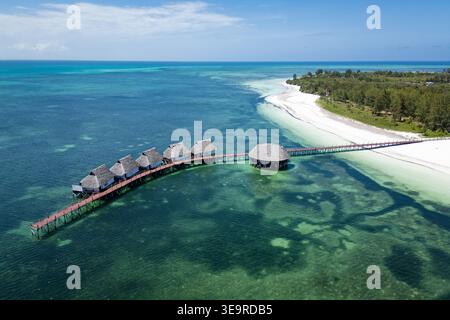 Vista aerea dei lussuosi bungalow sull'acqua con tetti di paglia e un molo di legno circondato dall'oceano color smeraldo e dalla spiaggia di sabbia bianca a Zanzibar. Foto Stock