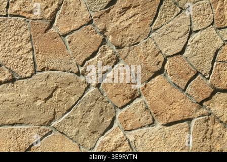 Parete in granito, sfondo, texture. Superficie in muratura caotica di grandi rocce granitiche di colore terracotta. La struttura murale delle pietre vulcaniche marroni. Mod Foto Stock