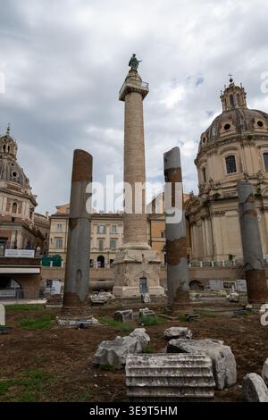Colonna Traiana nel foro Traiano, Roma, con le antiche colonne di marmo circostanti e le rovine sotto un cielo coperto. Foto Stock
