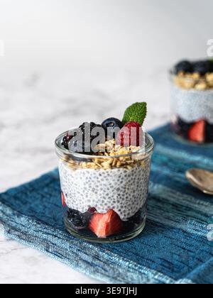 Vista frontale del chia parfait con frutti di bosco e muesli su un panno blu con cucchiaio e fondo sfocato Foto Stock