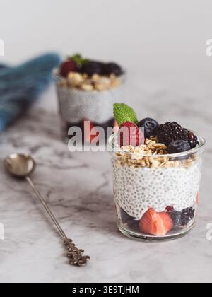 Primo piano verticale del budino di chia ricoperto di frutta e granola su sfondo di marmo chiaro Foto Stock