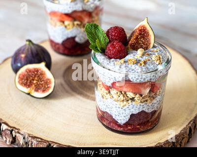Composizione frontale ravvicinata del pudding di chia parfait con fichi frutti di bosco e granola su fetta di legno Foto Stock
