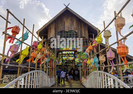 PATTAYA, THAILANDIA - 19 DICEMBRE 2023: Persone che camminano su un ponte che conduce a un tempio tradizionale in legno con vetrate colorate Foto Stock