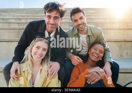 Un gruppo di quattro allegri amici abbracciano la loro amicizia mentre ridono e posano giocosamente per la fotocamera, catturando un momento di gioia e connessione Foto Stock