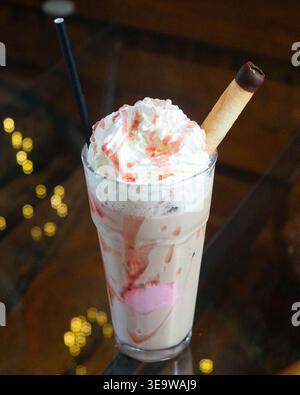 Bevanda cremosa con panna montata e gocciolamento di fragole. Le bacche di fragola si mescolano con il latte e la base per gelato. Bastoncino di cioccolato e Black Straw com Foto Stock