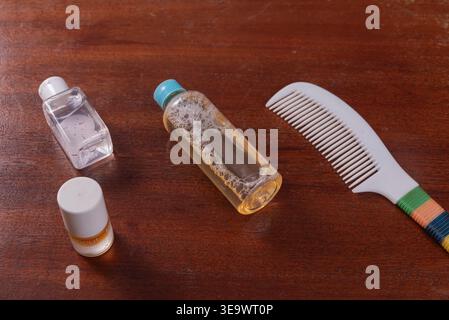 Prodotti per la cura dei capelli su superfici in legno invecchiate. I flaconi sono caratterizzati da liquidi e bolle trasparenti, pettine con dettagli colorati. Ripresa con luce diffusa. Concetto di Foto Stock