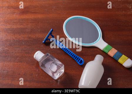 STILL Life con un rasoio blu, uno specchio e delle bottiglie su una superficie in legno. Luce soffusa e diffusa. Si concentra sulla cura della persona. Mette in risalto la pulizia e lo sci Foto Stock