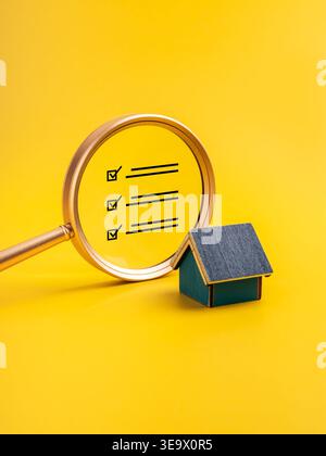 Concetto di ispezione della proprietà con lente d'ingrandimento e checklist vicino al modello della casa su giallo. Verifica della casa, audit immobiliare, controllo di qualità, saf Foto Stock