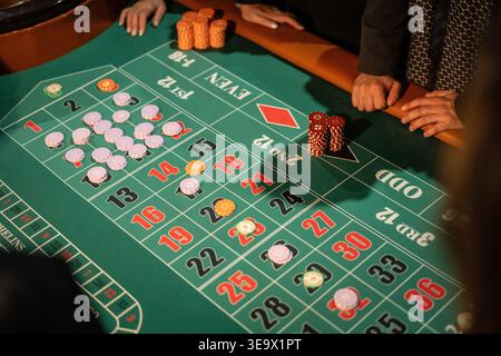 Gruppo di persone che piazzano scommesse con chip su un tavolo da roulette in un ambiente da casinò. Strategia di gioco d'azzardo, rischio, possibilità e scommesse. Foto Stock