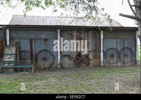 Fienile intempato con tetto in stagno e rivestimento blu arrugginito con vecchie ruote in legno e metallo appoggiate contro il lato dell'edificio Foto Stock