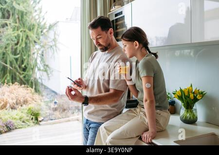 Papà con figlia con diabete in cucina a casa. Foto Stock