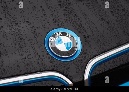 Kiev, Ucraina - 16 maggio 2025: Emblema della BMW i in bordatura blu sul cofano dell'auto elettrica modello i3 con gocce di pioggia. Foto Stock