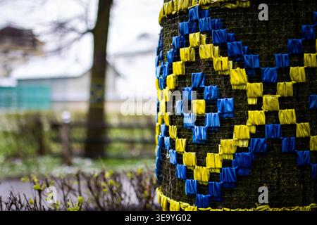 Le strisce blu e gialle brillanti intrecciano un audace motivo geometrico intorno al palo del parco. La pellicola realizzata a mano aggiunge una texture allegra a a una giornata grigia Foto Stock