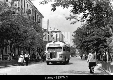Sloviansk, 1956-1960, via Shevchenko. Questa affascinante fotografia d'archivio storica presenta una vista posteriore dinamica di un classico autobus cittadino ZIS-155 che scende lungo un ampio viale. La parte posteriore arrotondata del veicolo, i finestrini sporgenti e la targa sono chiaramente visibili. Lussureggianti alberi verdi e eleganti lampioni stradali fiancheggiano i marciapiedi ben tenuti. Sullo sfondo, l'imponente facciata di un edificio residenziale a più piani mette in risalto lo sviluppo architettonico urbano e la vita serena nella tranquilla Donbas. Foto Stock