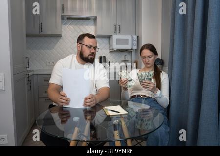 Coppia che esamina i documenti finanziari e conta il contante, affrontando sfide di budget e stress economico mentre si occupa delle spese domestiche nel loro modo migliore Foto Stock