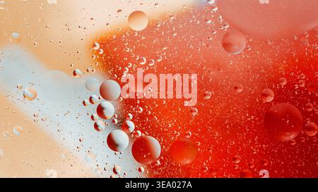 Goccioline d'olio e miscelazione dell'acqua, formando sfere colorate e un motivo astratto con sfumature di rosso, arancione e bianco. Fotografia in Thailandia, nessuna gen Foto Stock