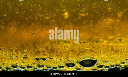 Le goccioline d'olio giallo oro che galleggiano nell'acqua creano texture astratte vivide e modelli circolari di liquidi immiscibili. Fotografia, niente intelligenza artificiale generativa Foto Stock