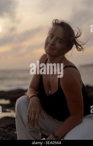 Donna serena con i capelli spazzati dal vento seduta sull'oceano al crepuscolo, Bali Foto Stock
