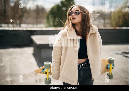 Bella donna con skateboard in piedi sul tetto dell'edificio Foto Stock