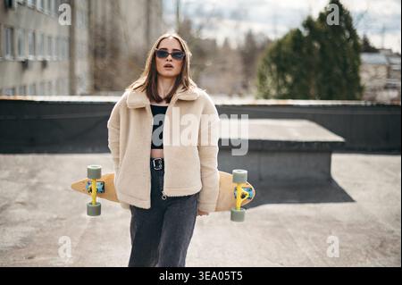 Bella donna con skateboard in piedi sul tetto dell'edificio Foto Stock