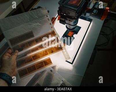 Telecamera mirrorless per la digitalizzazione dei negativi della pellicola apparecchiature da laboratorio light box. Fotografo professionista che tiene a mano strisce negative da 35 mm, manicotto in vetro Foto Stock