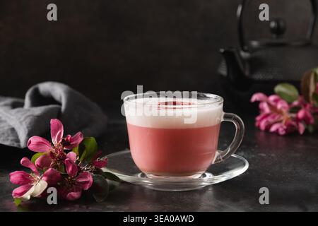 Latte matcha rosa con fiori sakura decorati a polvere su sfondo nero scuro. Bevanda alla moda. Senza caffeina. Primo piano. Foto Stock