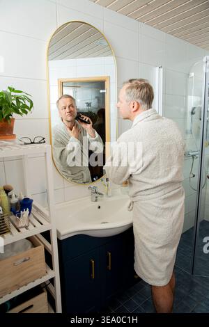 Rasatura dell'uomo con rasoio elettrico in un bagno luminoso e moderno, cura del corpo maschile, concetto di routine mattutina per la cura della persona e il benessere Foto Stock