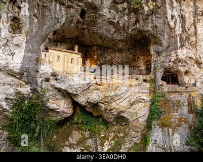 Vista aerea del Santuario de Covadonga, una basilica immersa in una grotta, dove la luce calda contrasta con la pietra grezza grigia, Santa Cueva de CoV Foto Stock