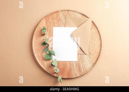 Busta con cartoncino vuoto e ramo di eucalipto su vassoio di legno, vista dall'alto. Biglietto d'auguri, piatto, mockup Foto Stock
