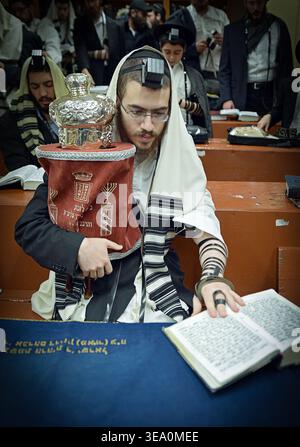 Un adoratore che tiene una piccola Torah durante le preghiere mattutine nei giorni feriali presso la sede centrale di Chabad Lubavitch a Brooklyn, New York Foto Stock