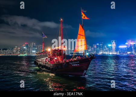 L'Aqua Luna II naviga di notte sul Victoria Harbour di Hong Kong durante lo spettacolo di laser Symphony of Lights con skyline illuminato sullo sfondo. Foto Stock