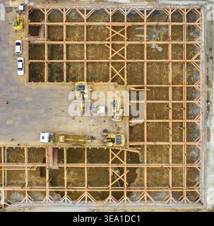 Vista aerea della costruzione di fondamenta con una griglia di travi di supporto e escavatori gialli in un cantiere a Taiwan. Foto Stock