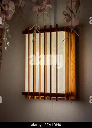 La lanterna in legno è appesa a una parete testurizzata. La luce soffusa filtra attraverso i pannelli in vetro smerigliato. I fragranti fiori rosa incorniciano la lanterna. Design tradizionale A. Foto Stock