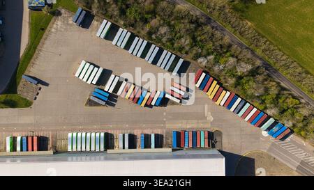 Vista aerea di container e rimorchi colorati parcheggiati in un centro di distribuzione logistica con magazzini e campi verdi Foto Stock