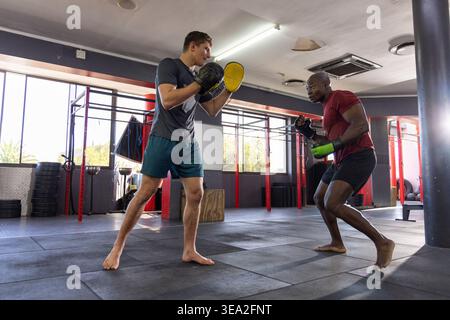 Diversi partner maschili di abbigliamento sportivo che praticano scioperi su tappetini da palestra con guanti da fuoco Foto Stock