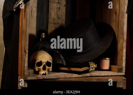 Una collezione raccapricciante di decorazioni di Halloween, tra cui teschi, un cappello da strega e un libro vintage disposto su una rustica mensola in legno Foto Stock