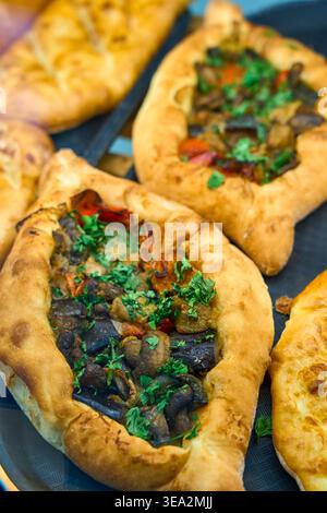 Dolci appena sfornati a forma di barca conditi con funghi, verdure ed erbe aromatiche. In mostra il tradizionale khachapuri georgiano o il pide turco. Foto Stock