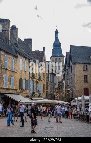 SARLAT-LA-CANEDA, FRANCIA, 01 AGOSTO 2025, la vivace piazza principale del mercato con edifici storici in pietra e il campanile della cattedrale nel centro di Foto Stock