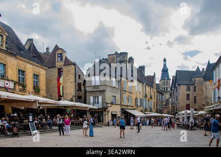 SARLAT-LA-CANEDA, FRANCIA, 01 AGOSTO 2025, la vivace piazza principale del mercato con edifici storici in pietra e il campanile della cattedrale nel centro di Foto Stock