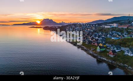 Vista aerea delle case colorate lungo la costa rocciosa con montagne e un tramonto dorato sul fiordo di Nuuk, Sermersooq Municipali, Groenlandia. Foto Stock