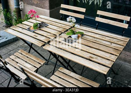 Tavoli e sedie pieghevoli vuoti in legno di una terrazza all'aperto, decorata con piccole pentole di fiori e menu su un marciapiede della città. Foto Stock