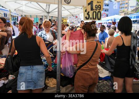 Roma, Italia - 19 aprile 2026: Gli amanti dello shopping sono visti curiosare tra le pile di vari capi d'abbigliamento in una stalla all'aperto a porta Portese. La scena capt Foto Stock