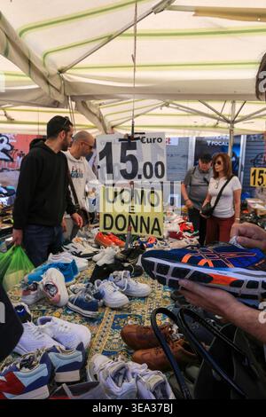 Roma, Italia - 19 aprile 2026: Vista ravvicinata di una bancarella di calzature al mercato delle pulci di porta Portese. I clienti vengono visti ispezionare vari modelli di sn Foto Stock