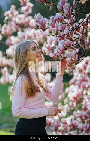 Giovane donna che gode della fioritura primaverile, dello sfondo floreale e dell'atmosfera morbida e romantica. Foto Stock
